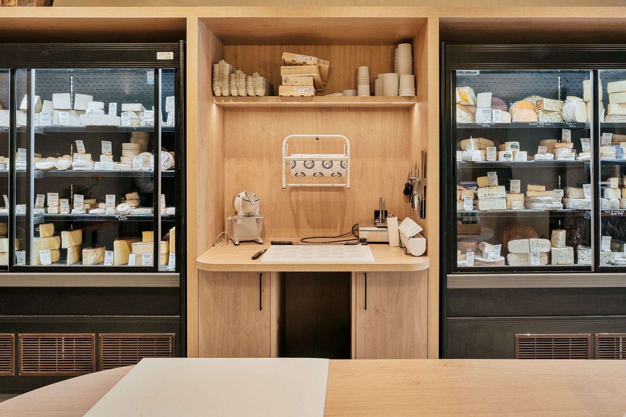 Chez les fromagers malouins, à Saint-Servan création d'une table de découpe centrale et d'un linéaire de présentation avec LED intégrées en mélanine et stratifié chêne. par Hugo Pauchard - HP Bois Menuiserie - Saint-Malo