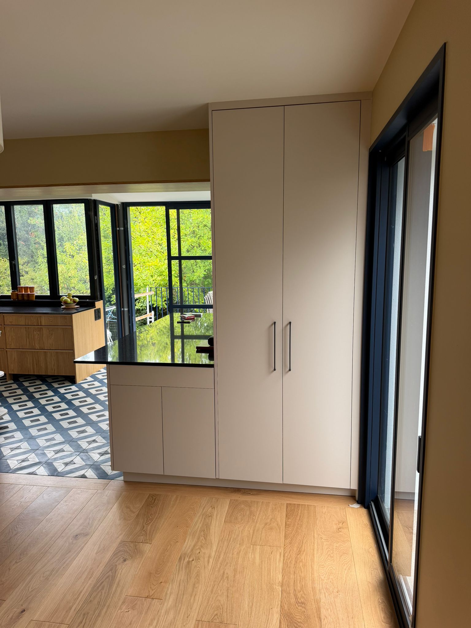 Nouvelle réalisation d'une cuisine sur mesure près de Saint-Malo, pensée pour conjuguer l'authenticité du bois et la modernité des touches de noir et de carrelage géométrique. Ses espaces dédiés et son ouverture sur l’extérieur en font un lieu de vie aussi pratique qu'esthétique au quotidien. - CCM Agencement - Saint-Malo